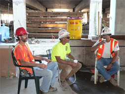 Men sitting down and drinking water in shaded area