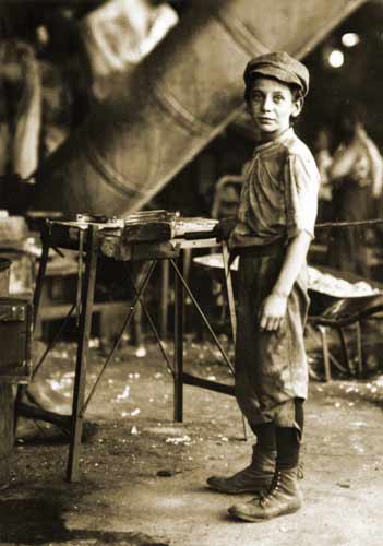 Photo of a child laborer stading in a metal shop, taken in the US in the early 20th century.